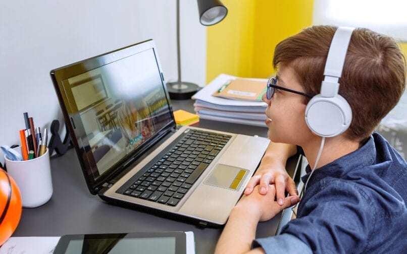Estudiante asistiendo a una clase en línea con unos auriculares blancos